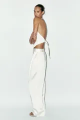 Pantalón blanco de tela satinada, tiro alto, corte ancho y pliegues en la parte delantera y trasera.