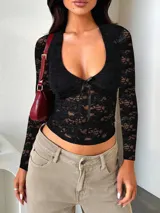 Top negro de encaje con escote en forma de corazón, mangas largas y lazo decorativo en el centro del busto.