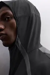 Chaqueta deportiva negra con paneles grises en hombros y laterales, capucha ajustable, cierre frontal con cremallera, bolsillos laterales con cremallera y puños elásticos. Zara Athleticz.