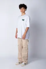 Remera blanca de corte oversize con mangas cortas y cuello redondo. Estampado pequeño en el frente con letras verdes.