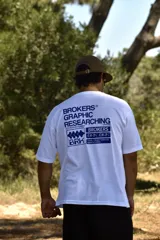 Remera blanca de manga corta con estampado gráfico en azul en la espalda, que incluye el texto "BROKERS GRAPHIC RESEARCHING" y varios logos de la marca.