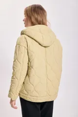 Campera capitoneada color verde claro, con capucha y cierre frontal con botones a presión. Tiene bolsillos laterales y cordón ajustable en el ruedo.