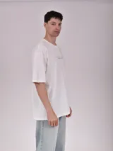 Remera blanca de corte recto con estampado de un auto clásico frente a un skyline urbano.