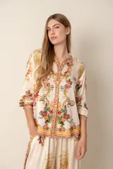 Blusa color crema con estampado floral y detalles de diseño barroco, con cuello mao, mangas 3/4 y cierre frontal con botones.