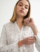 Camisa blanca de manga larga con tejido broderie (ojales bordados) y cuello camisero.