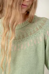 Sweater tejido color verde agua con cuello redondo y diseño de ochos con detalles rosados en la parte superior.