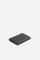 Cartera negra para pasaporte fabricada en piel, con tres posiciones para tarjetas y dos ranuras laterales.