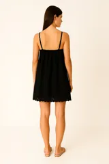 Vestido corto negro con breteles finos ajustables, escote profundo en V con borde festoneado y falda con detalle de bordado calado (broderie) en el ruedo.