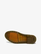 Bota Dr. Martens modelo 1460 de cuero marrón con aspecto desgastado y envejecido. Diseño de 8 ojales, con costuras amarillas, suela con amortiguación de aire resistente al aceite y lengüeta en el talón.