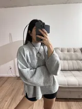 Sweater gris de tejido de punto grueso, con cuello alto, mangas anchas y aberturas laterales.
