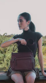 Cartera de cuero color borgoña, con correa larga regulable, dos bolsillos frontales con cierre y un bolsillo trasero con cierre.