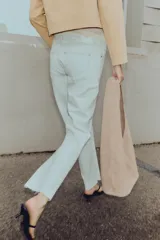 Jeans tobilleros de tiro alto color blanco, corte recto y bajo sin costura. Cierre frontal cruzado con cremallera y botones.