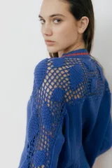Cárdigan azul con detalles en crochet, mangas con volado y vivos de color rojo en cuello, puños y frente. Tiene botones al frente.