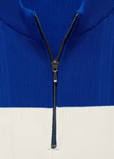 Top azul con panel blanco horizontal, cuello perkins y cierre de cremallera en el cuello.