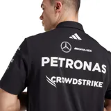 Polo oficial del equipo Mercedes-AMG Petronas Formula One Team, color negro, con cuello polo y botones frontales. Presenta detalles en blanco en los hombros y múltiples logos de patrocinadores en el pecho, incluyendo Mercedes-Benz, Petronas, INEOS, UBS, Crowdstrike, Snapdragon, TeamViewer, Hewlett Packard Enterprise y Signify.