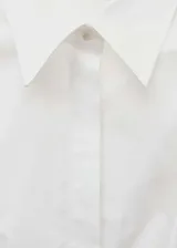 Camisa blanca de corte recto con cuello camisero, mangas largas con puños abotonados y cierre frontal oculto con botones.