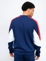 Buzo de felpa azul marino, con mangas largas, cuello redondo y puños acanalados. Presenta cortes en blanco y rojo en la parte superior, logo de Umbro bordado en el pecho y escudo del Club Nacional de Football.