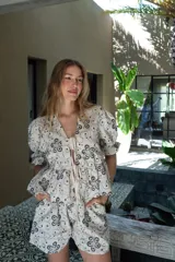 Blusa color crudo con estampado de flores negras, escote en V con lazos y mangas abullonadas.