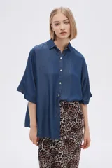Camisa de mangas cortas color azul denim, de corte holgado, con cuello camisero y cierre frontal con botones.