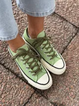 Zapatillas bajas de lona color verde claro, con cordones marrones, puntera de goma blanca y suela de goma blanca con línea negra.