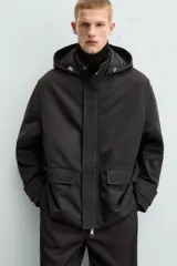 Parka negra de tejido técnico acolchado, corte regular fit, cuello alto con capucha ajustable, manga larga con puños ajustables, bolsillos de solapa en la cadera y bolsillo interior. Cierre frontal con cremallera oculta y botones a presión.