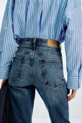 Pantalón de jean azul de tiro alto, corte mom fit, tobillero y con cinco bolsillos. Cierre frontal con cremallera y botón.
