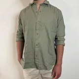 Camisa blanca de lino con corte regular, cuello clásico y mangas largas con puños abotonados.