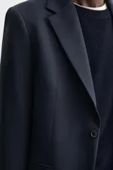 Blazer azul marino de corte recto confeccionado en tejido con lana. Tiene cuello con solapas de muesca, manga larga con puños abotonados, bolsillo de vivo en el pecho, bolsillos de solapa en la cadera, bolsillo interior y cierre frontal con botones.