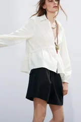 Camisa color crudo confeccionada con lino, de corte recto, cuello solapa con escote pico y manga larga. Presenta aplicación de pasamanería en el frente y cierre frontal con botones forrados a tono.