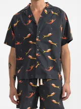 Short de algodón negro con estampado de sirenas color naranja y amarillo. Tiene cintura elástica con cordón ajustable, dos bolsillos laterales y un bolsillo trasero.