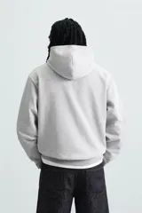 Sudadera con capucha color crudo, de corte relajado, confeccionada en tejido de algodón con interior rizado. Cuenta con cuello con capucha, manga larga, bolsillo frontal tipo canguro y acabados en rib.