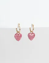 Aros tipo argolla dorados con dije de corazón cubierto de glitter rosa.
