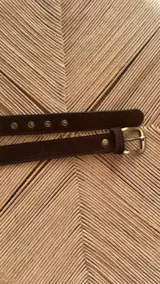 Cinturón negro de cuero sintético con hebilla cuadrada dorada y ojales metálicos.