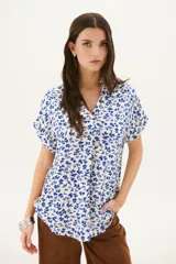 Blusa estampada con hojas azules sobre fondo blanco, con cuello en V y mangas cortas con dobladillo.