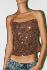 Top strapless color marrón, confeccionado en tejido tipo red con aplicación de strass y forro interior combinado. Presenta tejido drapeado y cierre en espalda con cremallera metálica.