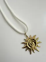 Collar con dije dorado en forma de sol con espiral central, colgando de una cuerda blanca.