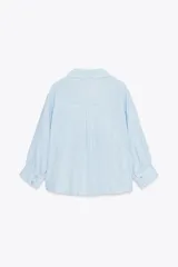 Camisa blanca de cuello solapa y manga larga con puños. Tiene un nudo en la parte delantera y cierre frontal con botones.