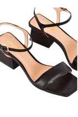 Sandalias de cuero negro con textura de piel de serpiente, tira ancha sobre los dedos, pulsera ajustable al tobillo con hebilla dorada y tacón geométrico de 6 cm.