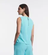 Blusa sin mangas color celeste, de crepé, con cuello redondo, pliegues en uno de los hombros y cierre trasero por cremallera con detalle de aro en el tirador.