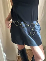 Cinturón negro de cuero sintético con hebillas circulares doradas.