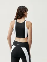 Top deportivo cropped bicolor negro con bandas blancas en los laterales, de sujeción media, con sujetador interior y logo en el pecho.