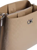 Cartera Calvin Klein tipo bucket color beige con monograma en relieve. Tiene correa ajustable para usar al hombro o cruzada, y cierre de cremallera.