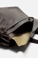 Bolso de mano extragrande color marrón oscuro, fabricado en piel de alta calidad. Tiene un compartimento principal con cierre magnético, un bolsillo interior con cremallera y un bolsillo secundario con solapa y cinta. Las asas son de piel.