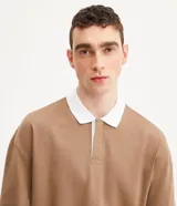 Remera polo de hombre color marrón, corte relaxed, confeccionada en media malla de algodón. Presenta cuello camisero blanco contrastante, tapeta con botones, mangas largas con sisa desplazada y puños ajustados.