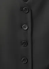 Chaleco negro con cierre de botones en la parte delantera, cuello de pico, sin mangas y dos bolsillos de ribete en la parte delantera.