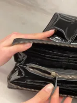 Billetera tipo clutch de cuero charol negro con cierre de cremallera y solapa con tres apliques piramidales.