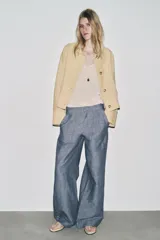 Pantalón de tiro bajo color azul con textura de lino, de pierna ancha, con bolsillos delanteros y traseros. Cierre frontal con cremallera, botón y ganchos metálicos.