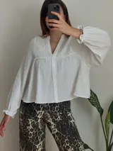 Camisa blanca de muselina con cuello en V, mangas largas abullonadas con puños elásticos y bordados en el canesú.