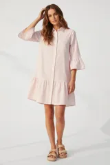 Vestido camisero corto de algodón a rayas verticales rosas y blancas, con cuello camisero, mangas 3/4 con volados y falda con volados. Cierre frontal con botones.