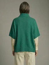 Capa o poncho tejido color verde esmeralda, con cuello polera alto que se cierra con un botón grande en el lateral. Presenta mangas cortas estilo japonesa y un calce amplio.